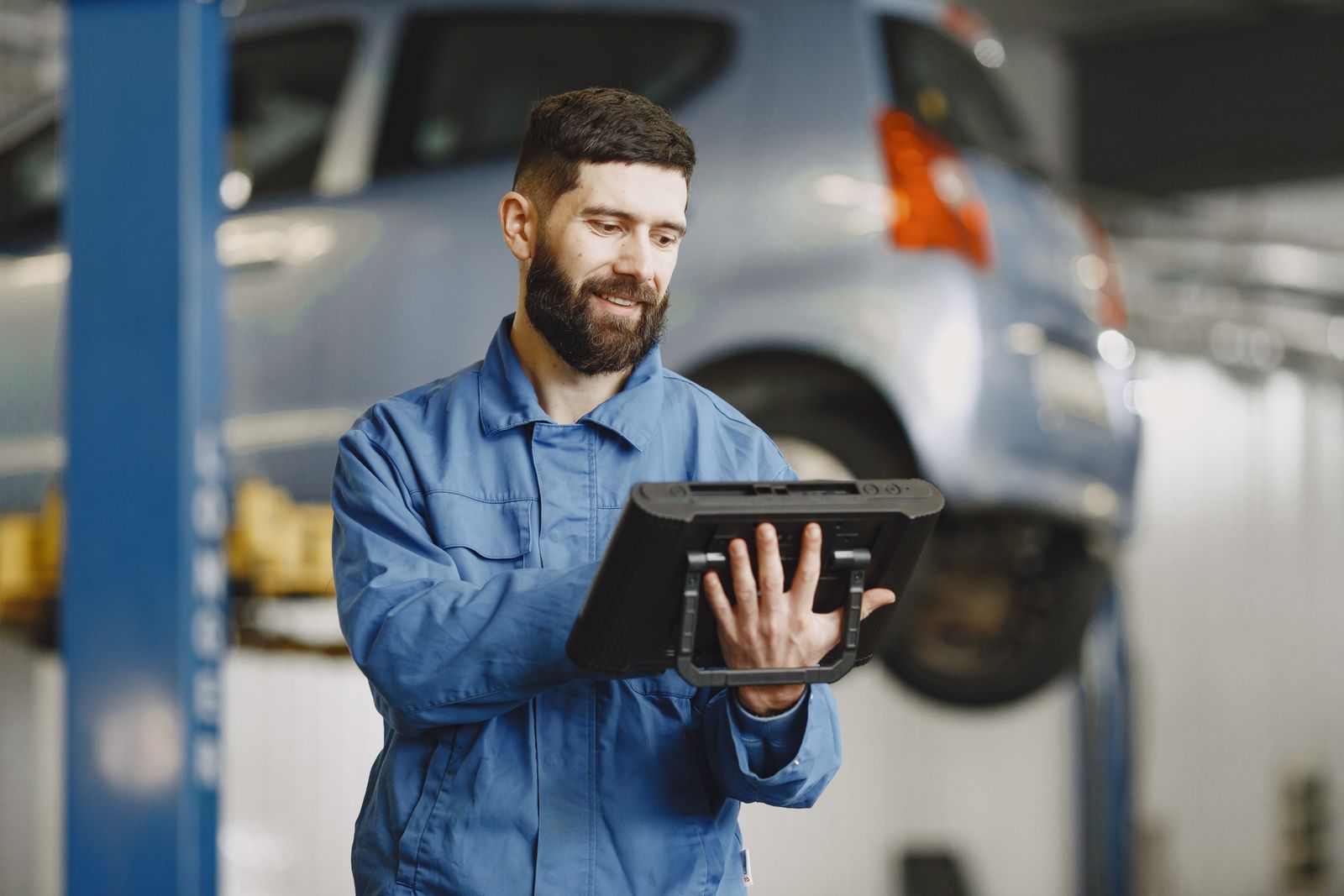 A mechanic checking a tablet beside a lifted car