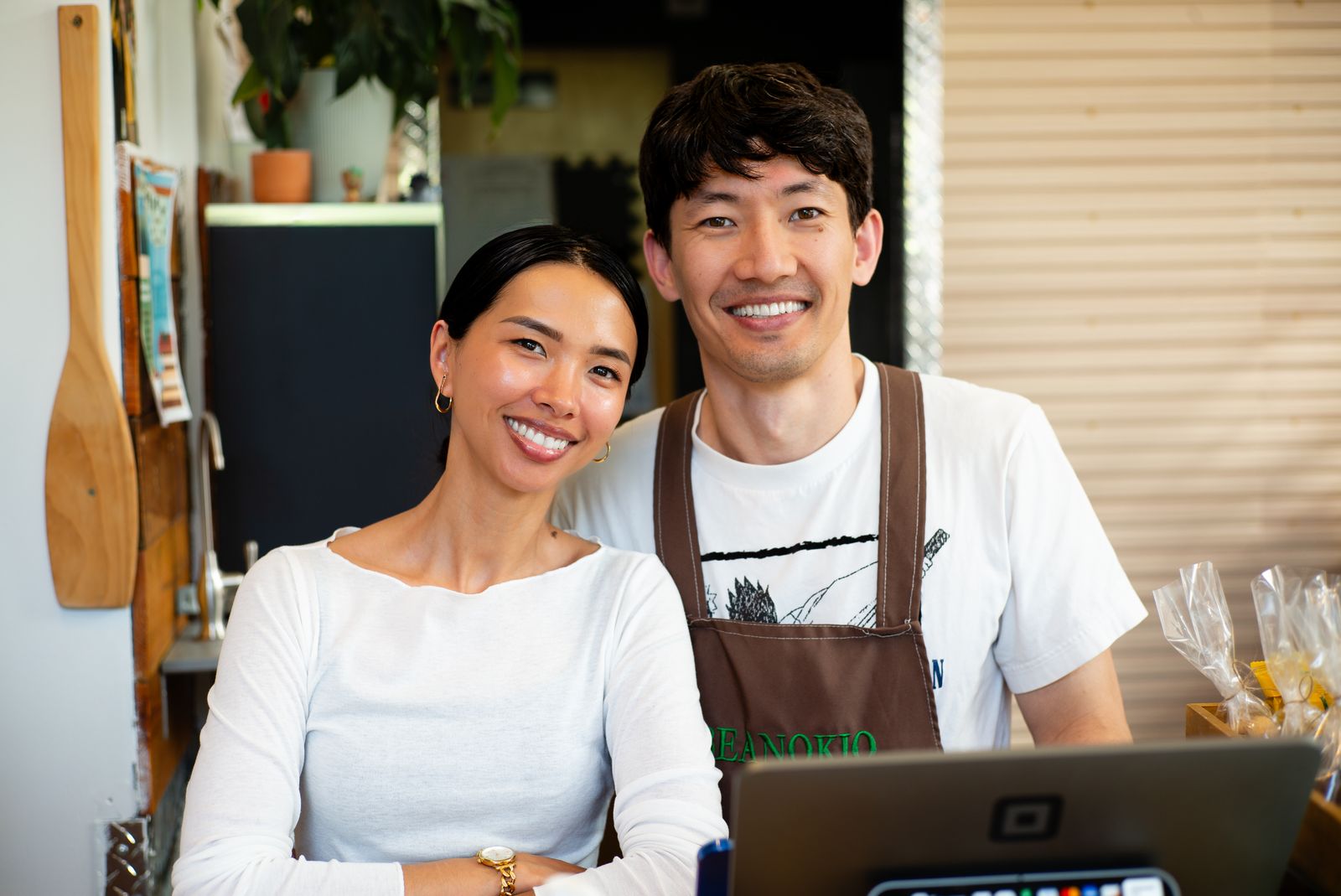 Two shop owners smiling at their counter with a laptop and card reader